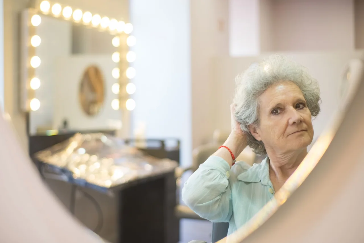 Mature woman checking her short grey hair in a salon mirror