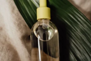 Clear cosmetic serum bottle with a dropper resting on a green leaf
