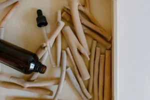 Amber dropper bottle beside pale wooden sticks on a neutral surface