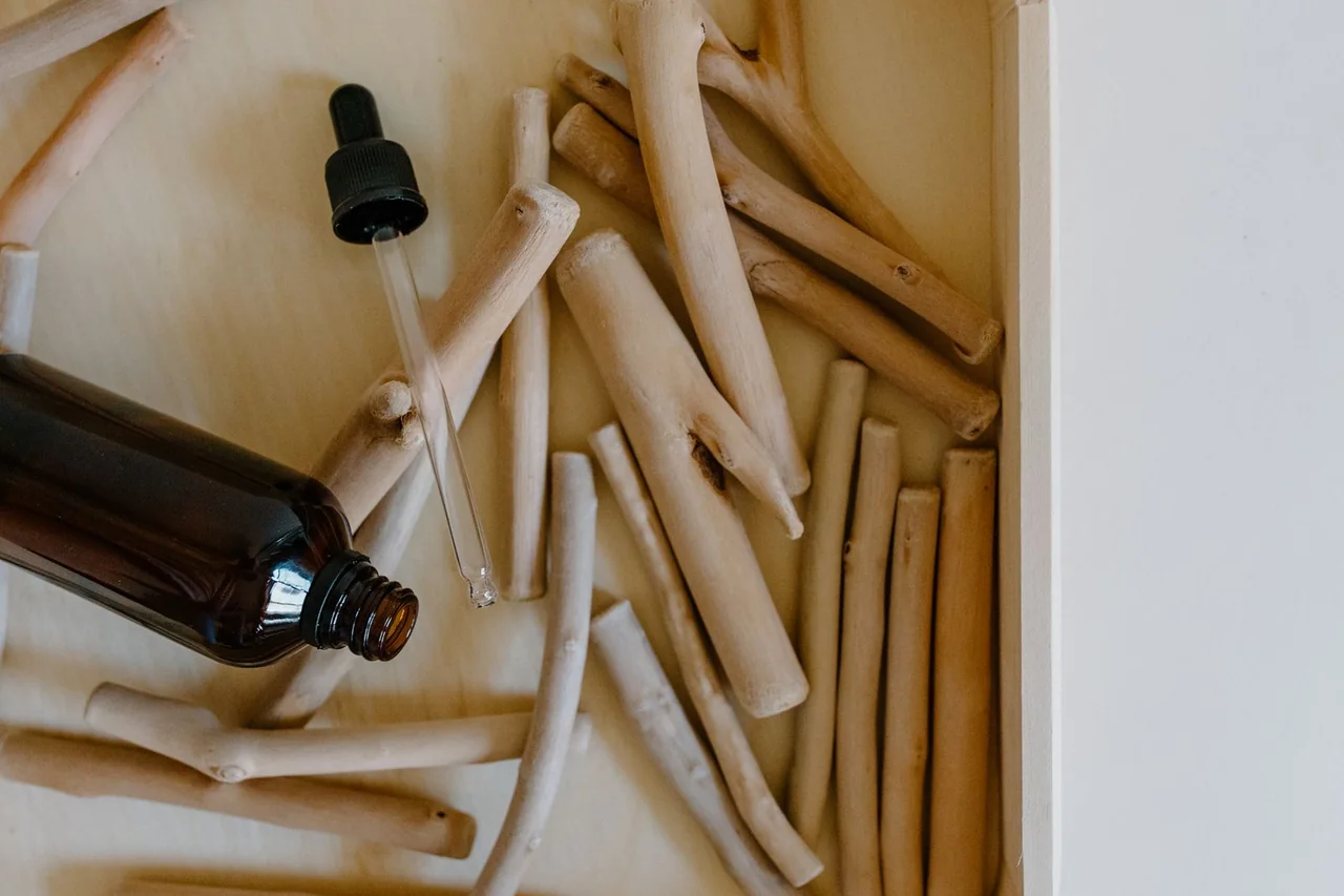 Amber dropper bottle beside pale wooden sticks on a neutral surface