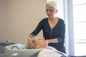 Hairdresser washing a mature woman’s hair at a salon basin