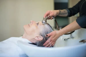 Close-up of grey hair being rinsed with a handheld salon sprayer