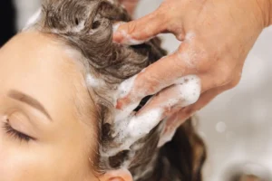 Hairdresser massaging shampoo through a woman’s hair at a wash basin
