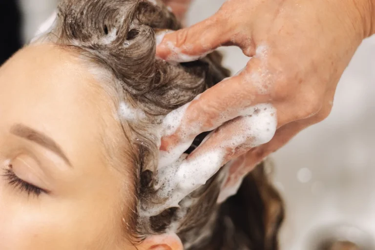 Hairdresser massaging shampoo through a woman’s hair at a wash basin