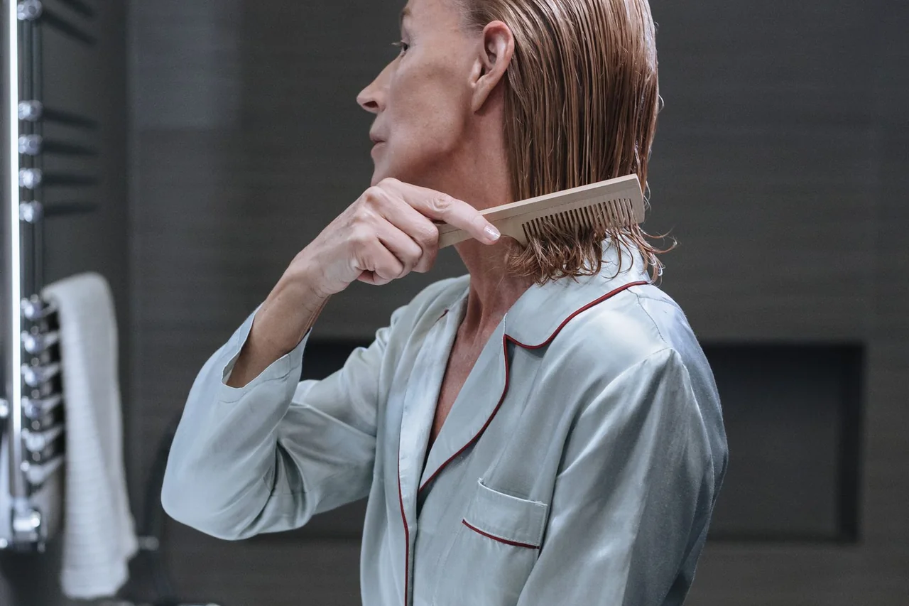 Mature woman gently combing her hair in a bathroom mirror